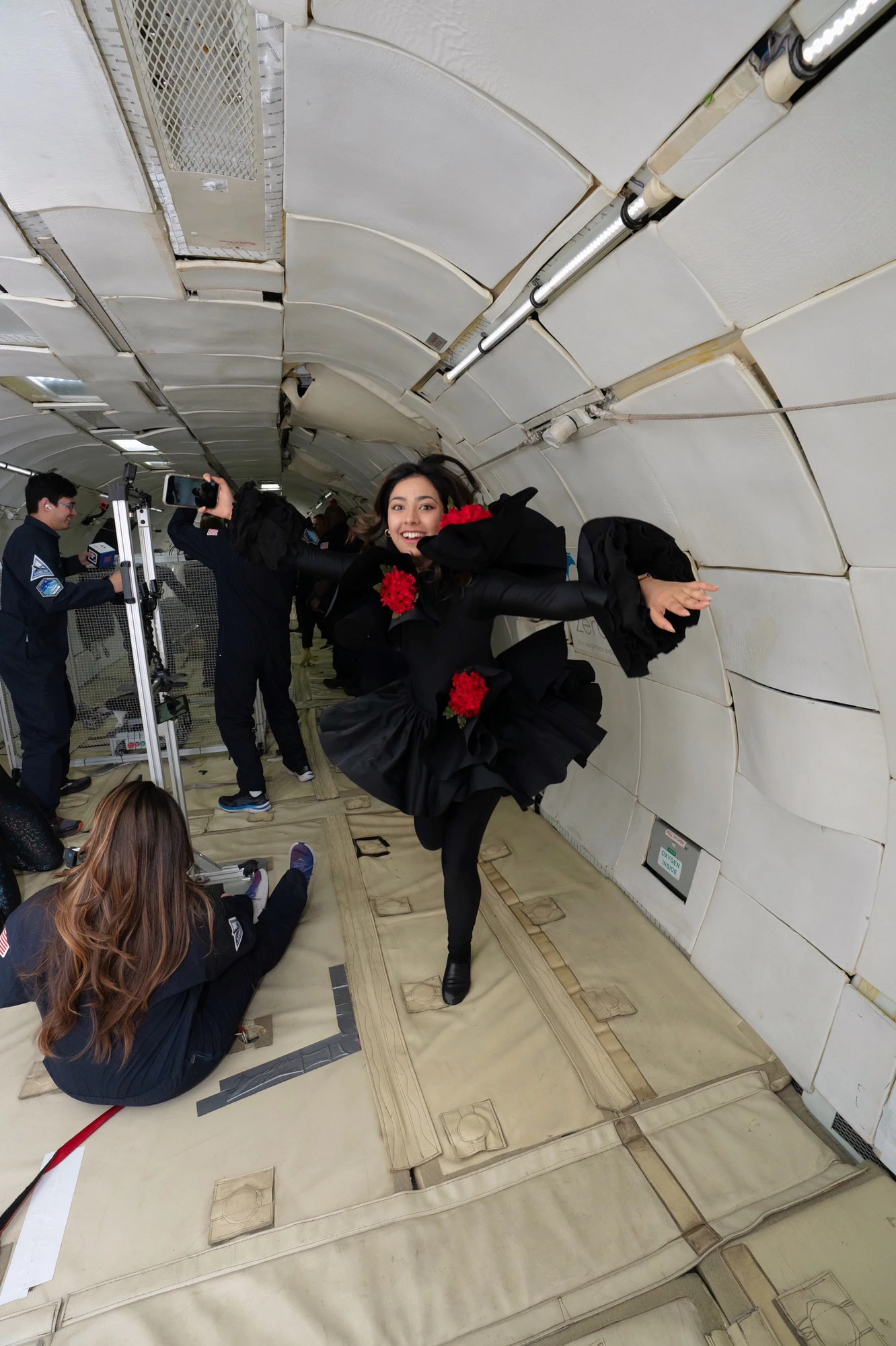 Jagriti floating with arms spread, red silk flowers blossoming outward in zero gravity